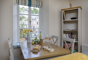 A dining table with a view of the outside, a bookshelf, and various food items. - Old Mill Court is a charming, dog-friendly two-bedroom cottage in Brixham (Brixham)