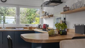A modern kitchen with a large window, a sink, a stove, and a countertop with a plant and a bowl of fruit. - Seaside Rendezvous is a bright, modern three-bedroom townhouse in Brixham (Brixham)