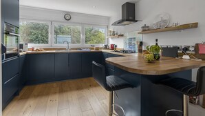 A modern kitchen with a central island, bar stools, a built-in oven, and a large window. - Seaside Rendezvous is a bright, modern three-bedroom townhouse in Brixham (Brixham)