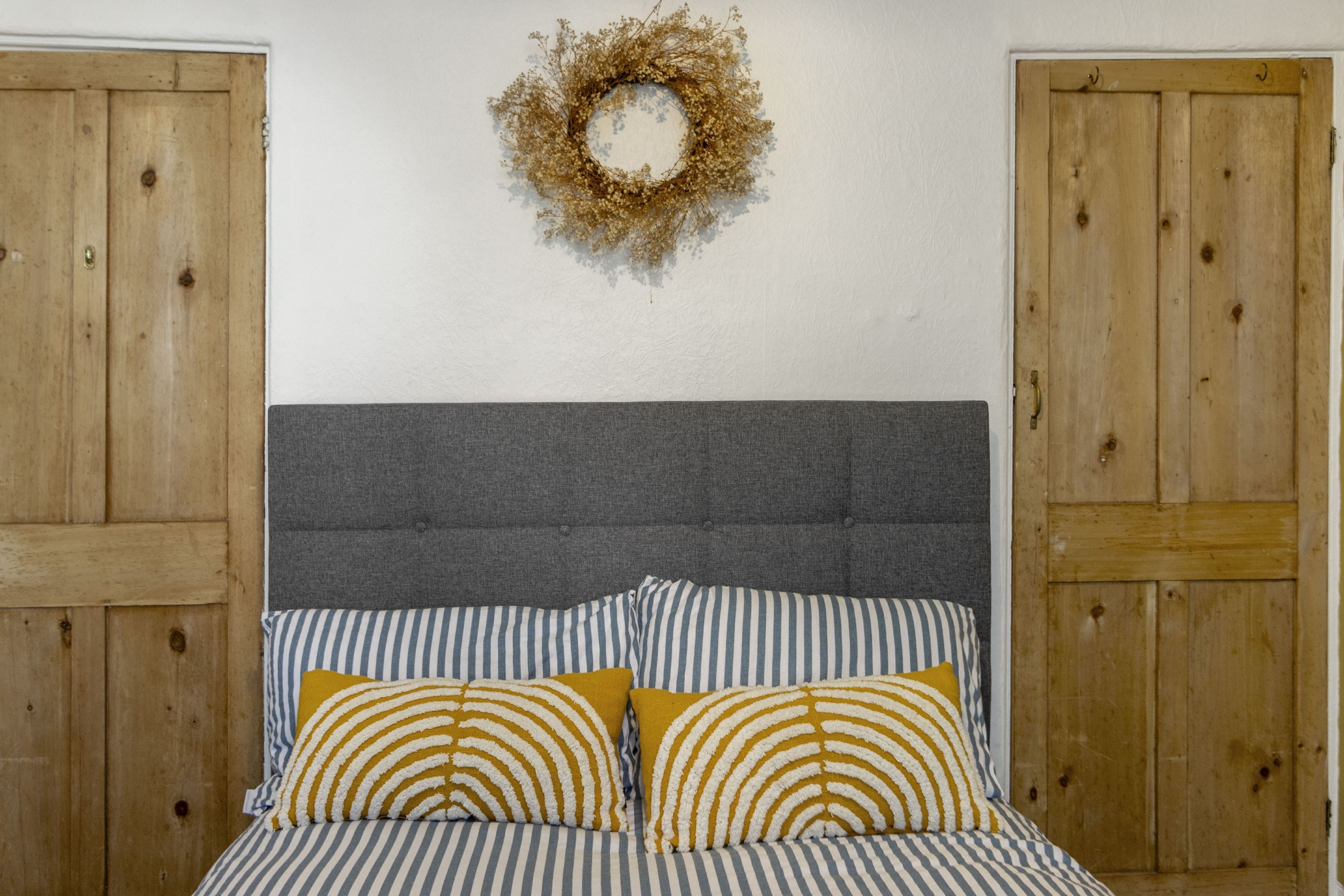 A bed with striped bedding and two pillows, a grey upholstered headboard, and a wooden door on the left.