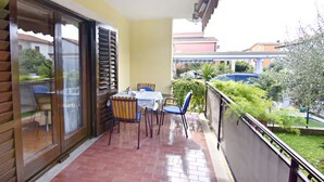 Un balcón con mesa y sillas, una puerta corrediza de vidrio y vistas a una piscina y vegetación.