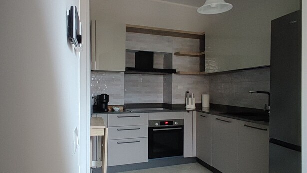 A modern kitchen with grey cabinets, a built-in oven, and a hanging light fixture.