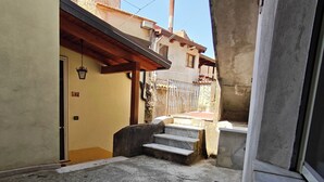 A narrow alleyway with a concrete ground, a set of stairs leading to a building entrance, and a visible door with a number.