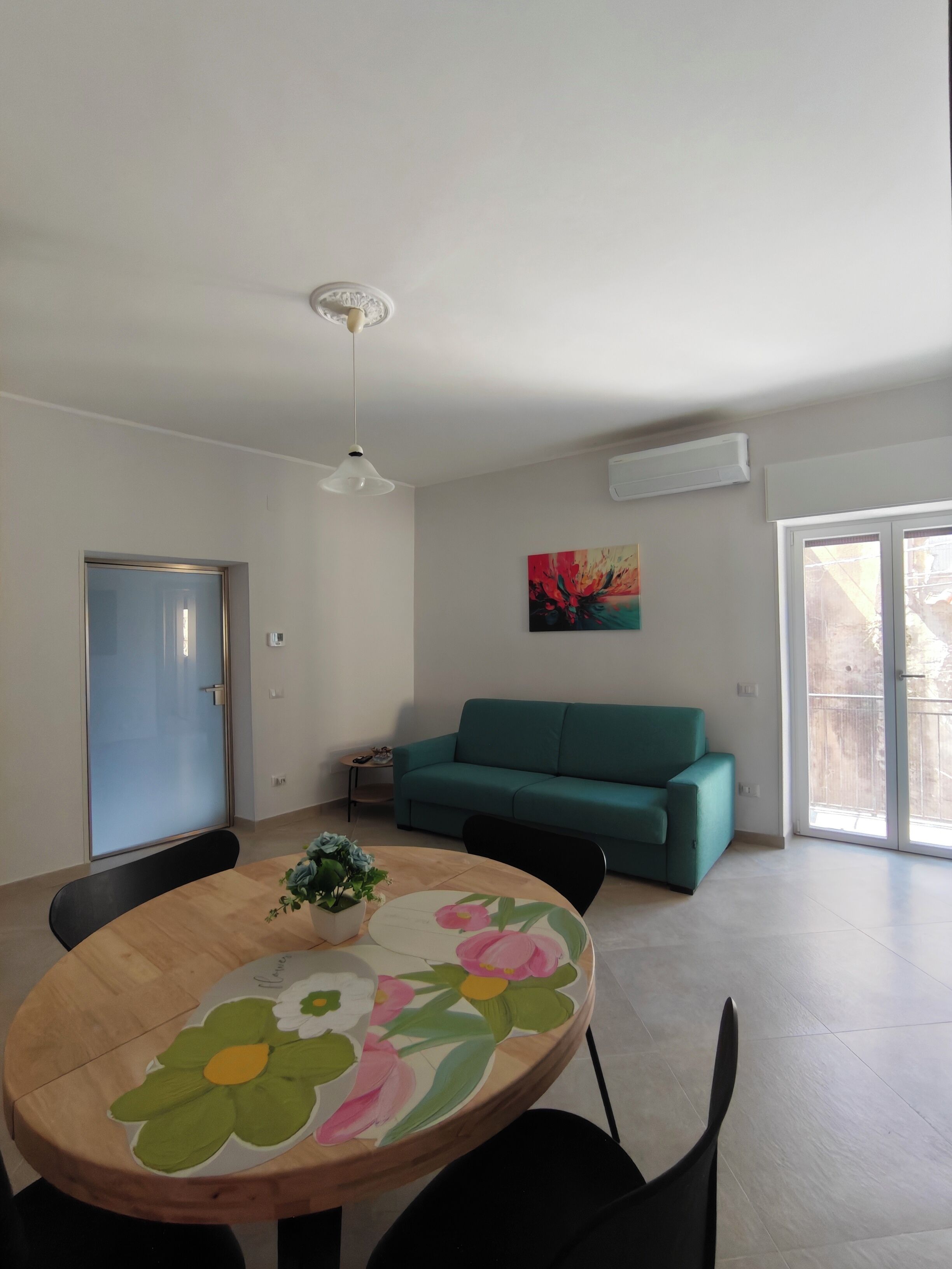Ein modernes Wohnzimmer mit einem runden Holztisch, einem blaugrünen Sofa und einem Deckenventilator.