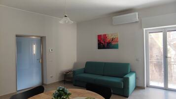 Ein modernes Wohnzimmer mit einem runden Holztisch, einem blaugrünen Sofa und einem Deckenventilator.