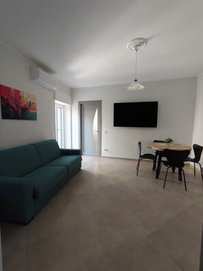 Uma sala moderna com um sofá verde-água, uma mesa de jantar com cadeiras, uma televisão de tela plana na parede e um ventilador de teto.