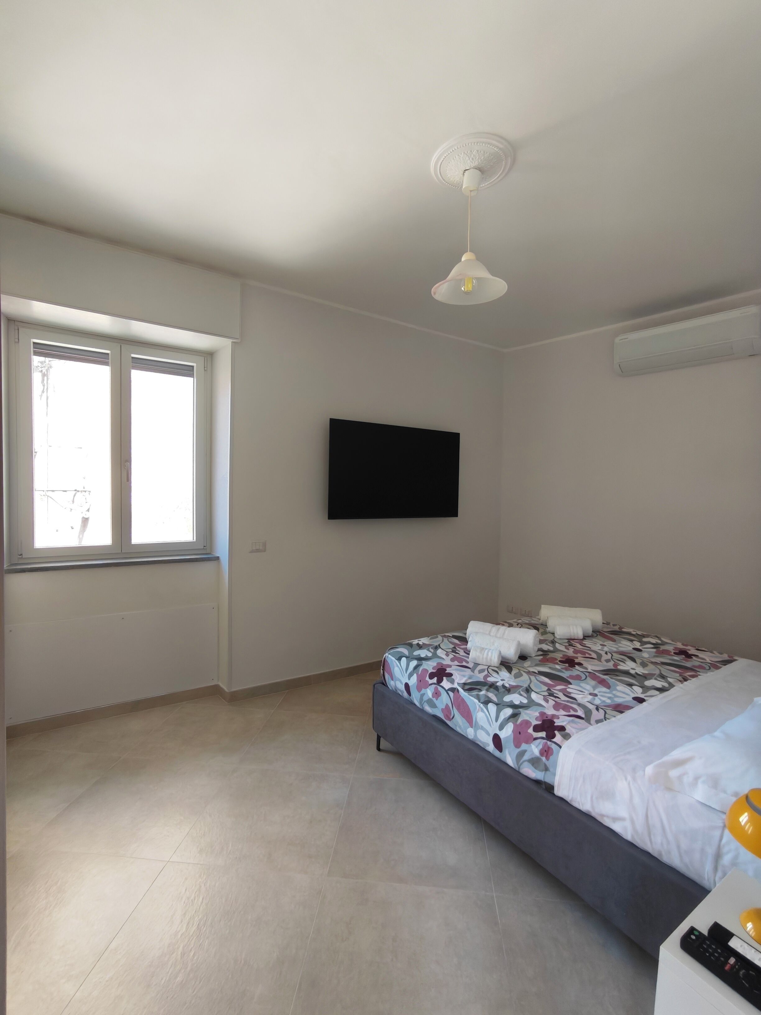 Un dormitorio con cama, televisor de pantalla plana, ventana y ventilador de techo.