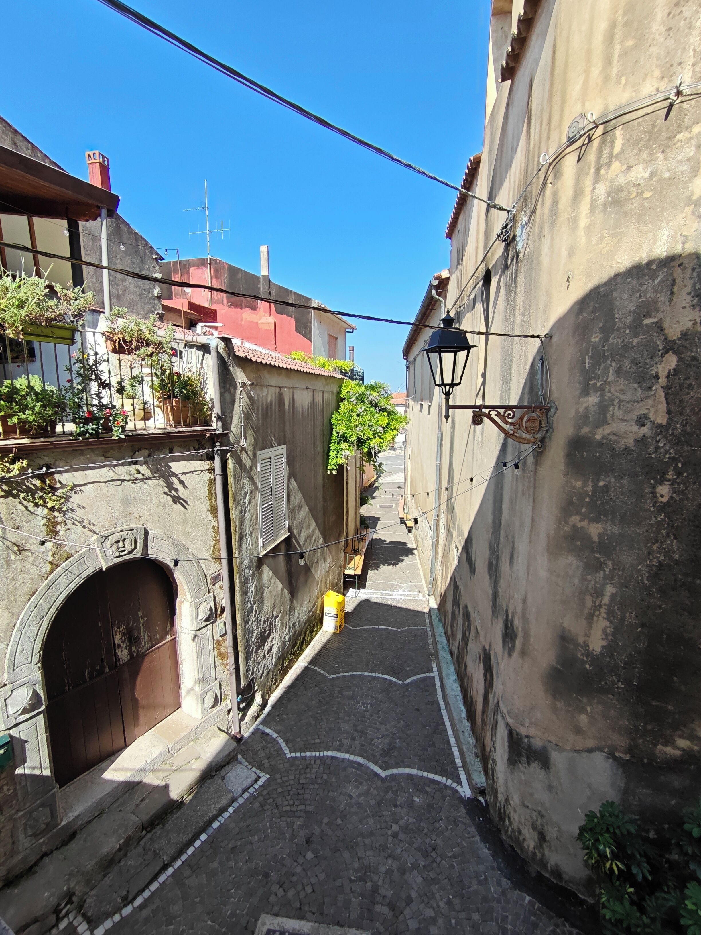 Une ruelle étroite pavée de pierres, un arc en pierre et un tonneau jaune.