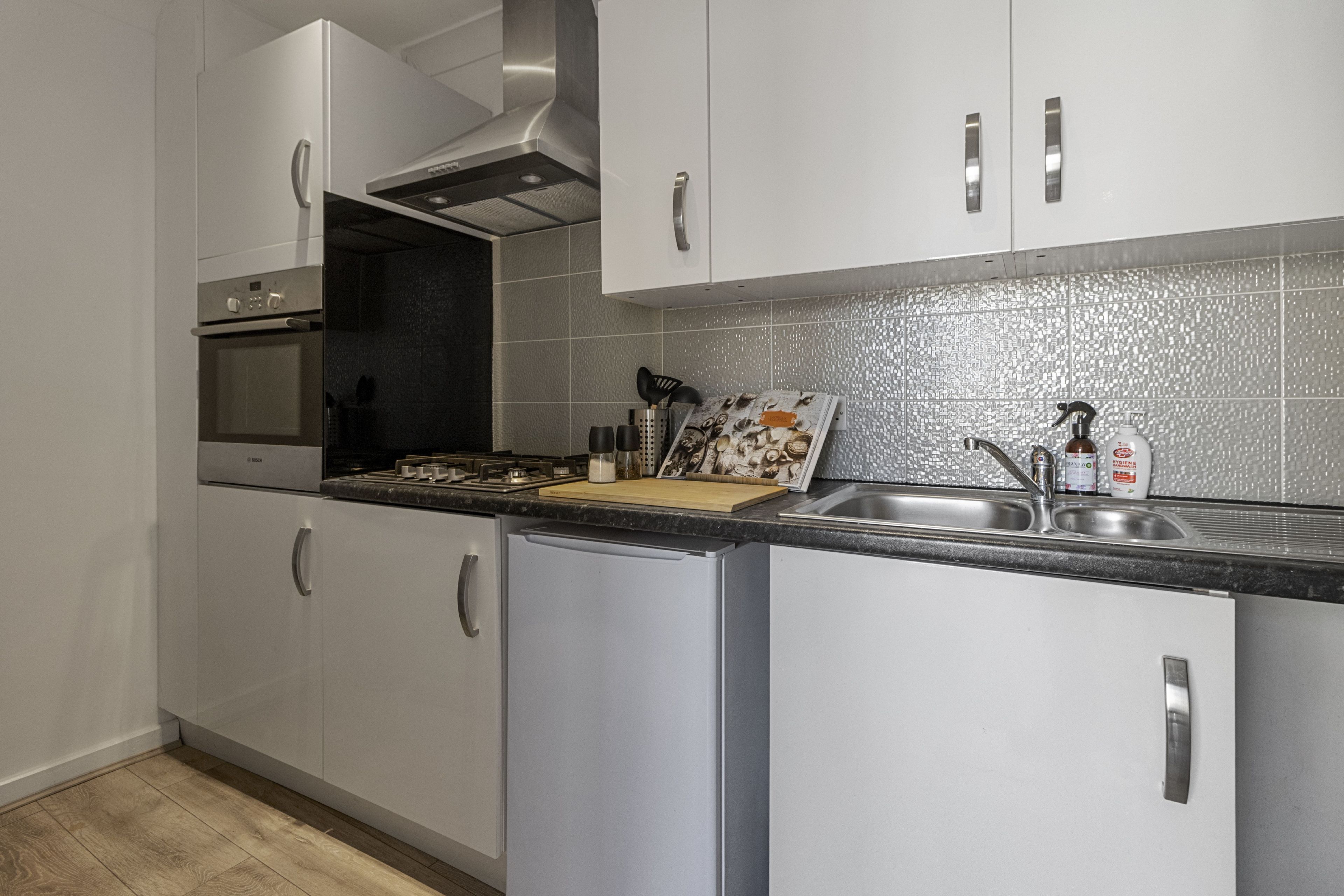 A modern kitchen with white cabinets, a stainless steel sink, and a built-in oven.