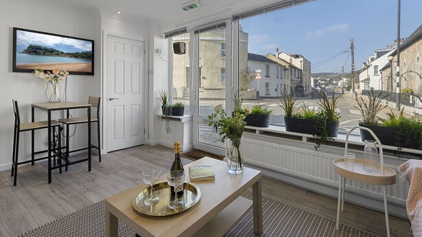 Una camera moderna con una grande finestra, un'area pranzo con tavolo e sedie, una TV a parete e vista sulla strada.