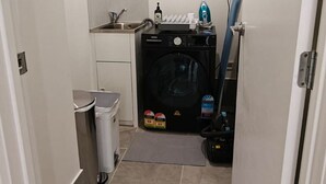Una cocina compacta con lavadora, un lavamanos y un cubo de basura.