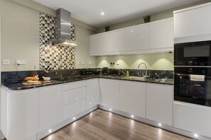 A modern kitchen with white cabinets, a black countertop, and a stainless steel range hood. - La Petite Maison is a dog-friendly waterfront dual-apartment in Brixham (Brixham)