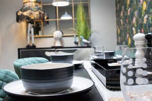 A dining area with a table set with plates, bowls, and glasses. There is a lamp, a mirror, and a decorative bird statue on the wall. - La Petite Maison is a dog-friendly waterfront dual-apartment in Brixham (Brixham)