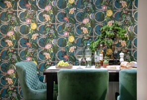 Un coin repas avec un papier peint à motifs, une table dressée avec une bouteille, des verres et un saladier de fruits.