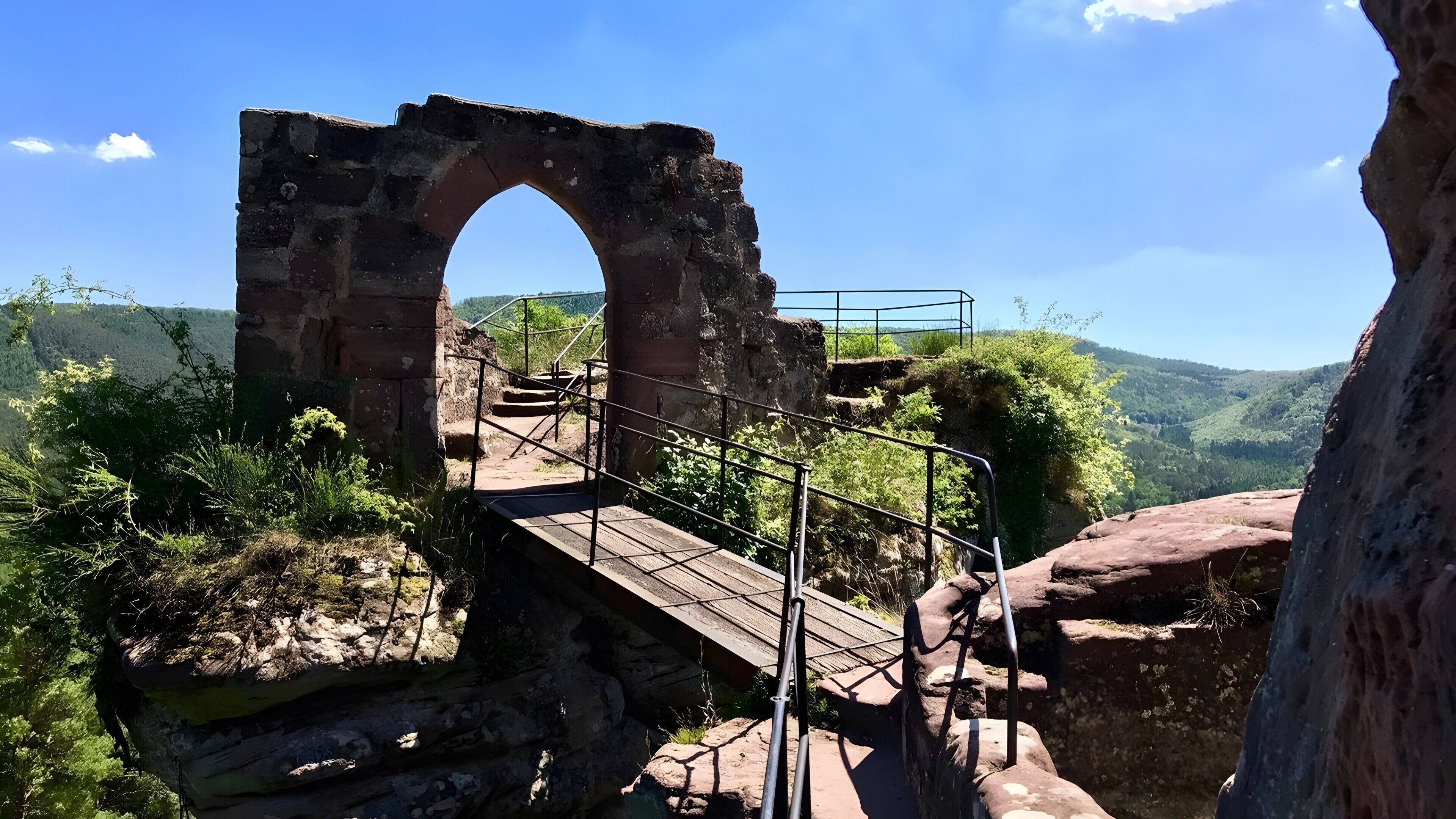 Un antiguo arco de piedra con un puente de madera que cruza terreno rocoso.