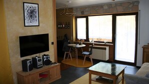 Un saló amb televisió de pantalla plana, màquina de cafè i zona de menjador amb taula i cadires.