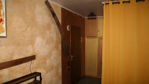 Una habitació amb una banca de fusta, una porta, un armari i una cortina groga.