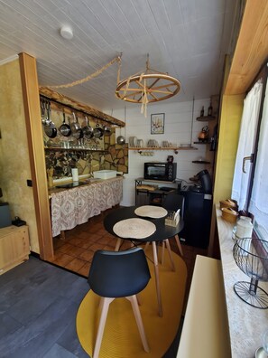 A compact kitchen with a stone backsplash, hanging pots, a microwave, and a dining area with two chairs and a table. - Apartment for 2 Guests (39 m²) in Ludwigswinkel (Dogs Welcome) (Ludwigswinkel)
