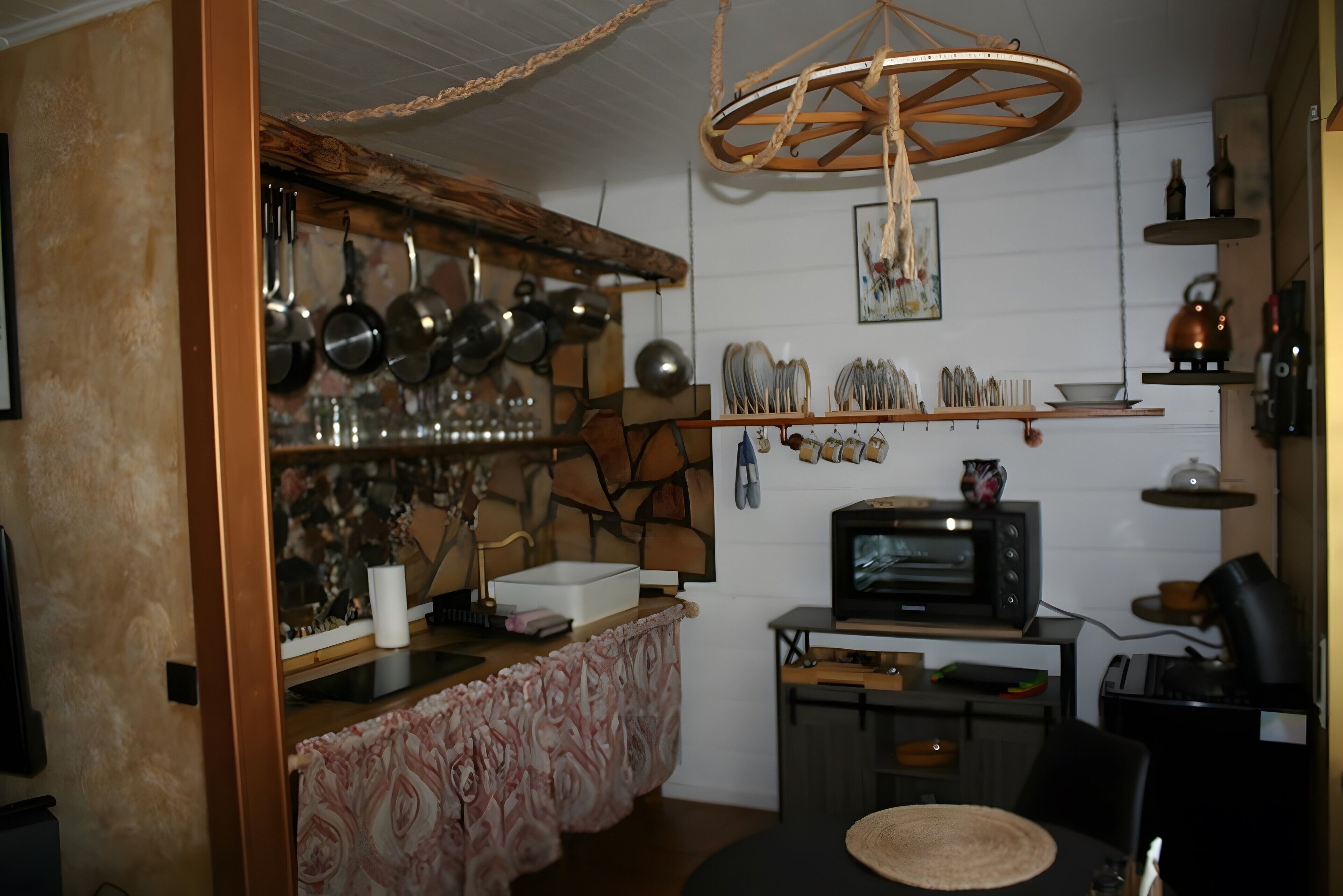 Una cocina compacta con protector de piedra, un colgador para ollas, un televisor antiguo y una lámpara rústica.