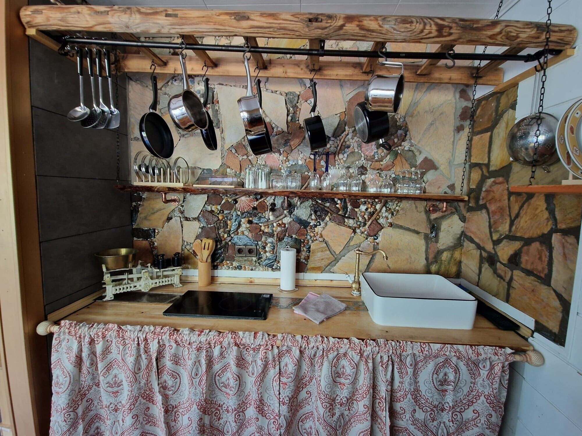 Una cocina rústica con ollas colgantes, un salpicadero de piedra y un mantel estampado.
