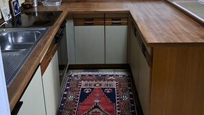 Keittiössä on puinen työtaso, pesuallas, kaappeja, kuviollinen matto ja seinällä koristeellisia lautasia.