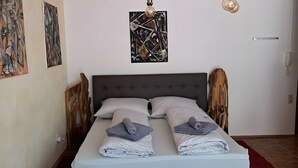 A neatly made bed with two pillows, a wall-mounted light fixture, and abstract art on the wall.