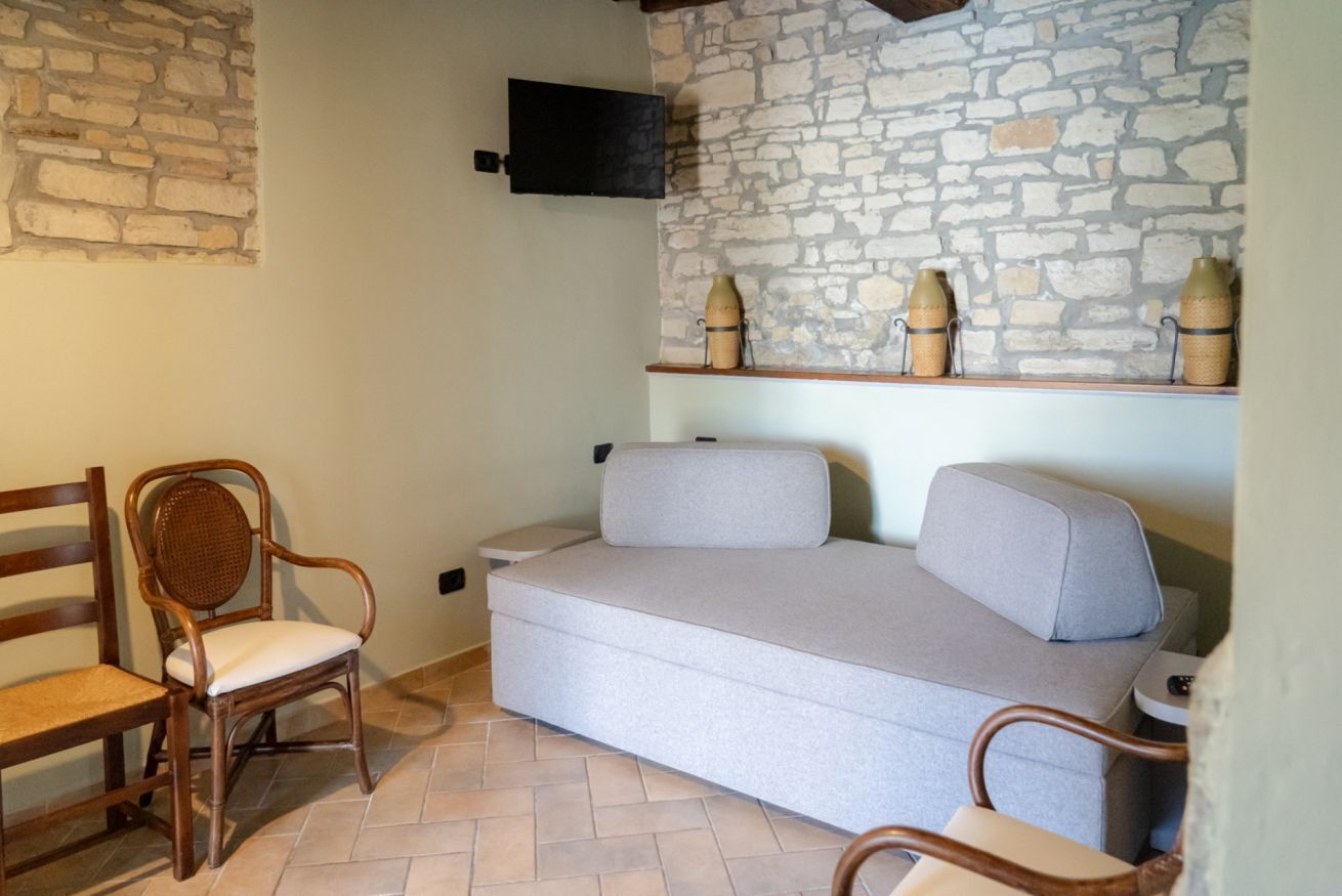 A room with a stone wall, a grey sofa, and wicker chairs.