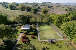 A tennis court surrounded by a well-maintained garden and a house with a white roof. - Villa Ippolito by MMega (Sant'Ippolito)