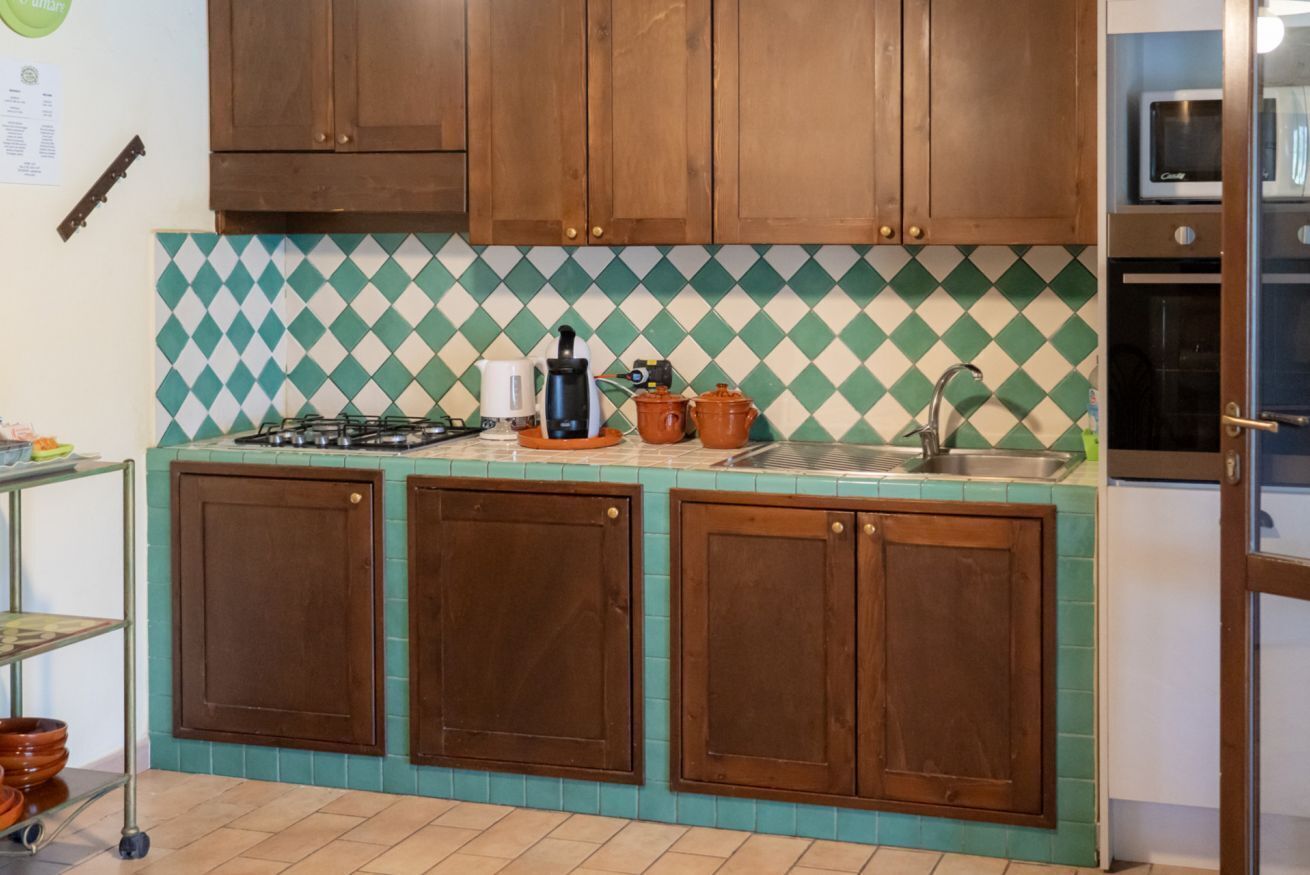 Een keuken met houten kastjes, een gasfornuis, een spoelbak en een magnetron.