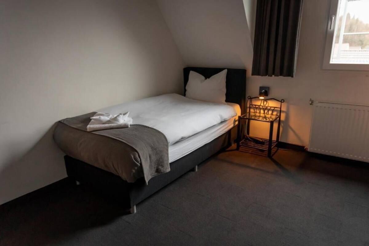 A single bed with a headboard, a bedside table with a lamp, and a window with curtains.