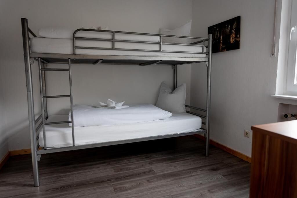 A bunk bed with a white mattress and pillows, a wooden desk, and a painting on the wall.