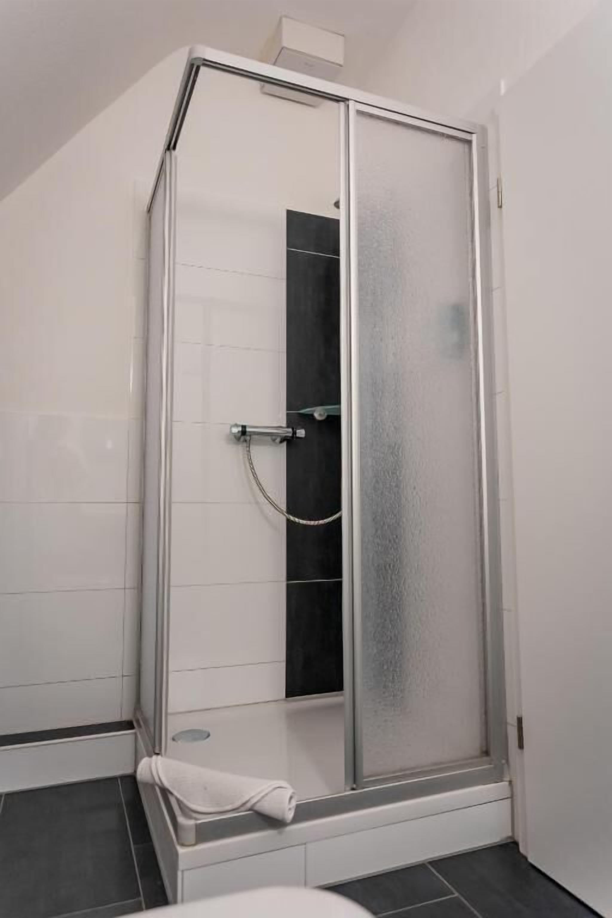 Eine Duschkabine mit Glastür, ein Handtuch auf dem Boden und eine weiße Fliesenwand.