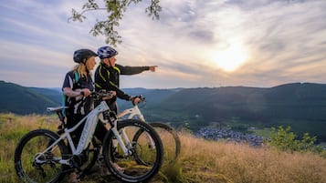 Dos personas en un sendero de bicicleta de montaña con una vista panorámica de un valle y un pueblo distante.