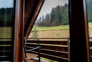 Un banco de madera con estructura metálica, con vista a un campo cubierto de hierba y una zona boscosa.