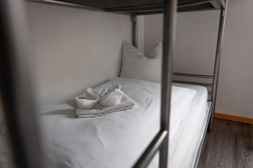 A bunk bed with white bedding and pillows, a metal frame, and a wooden floor.