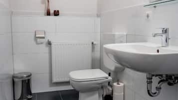 Et badeværelse med et hvidt toilet, en hvid vask, en brusekabine med glaslåger og et hvidt håndklædetørrestativ.