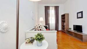 Ein modernes Wohnzimmer mit einer Couch, einem Fernseher, einem Bücherregal und einem Esstisch mit einer Pflanze.