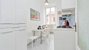 Eine moderne Küche mit weißen Schränken, einem Essbereich mit Tisch und Stühlen, einem Fenster und einer Uhr an der Wand.