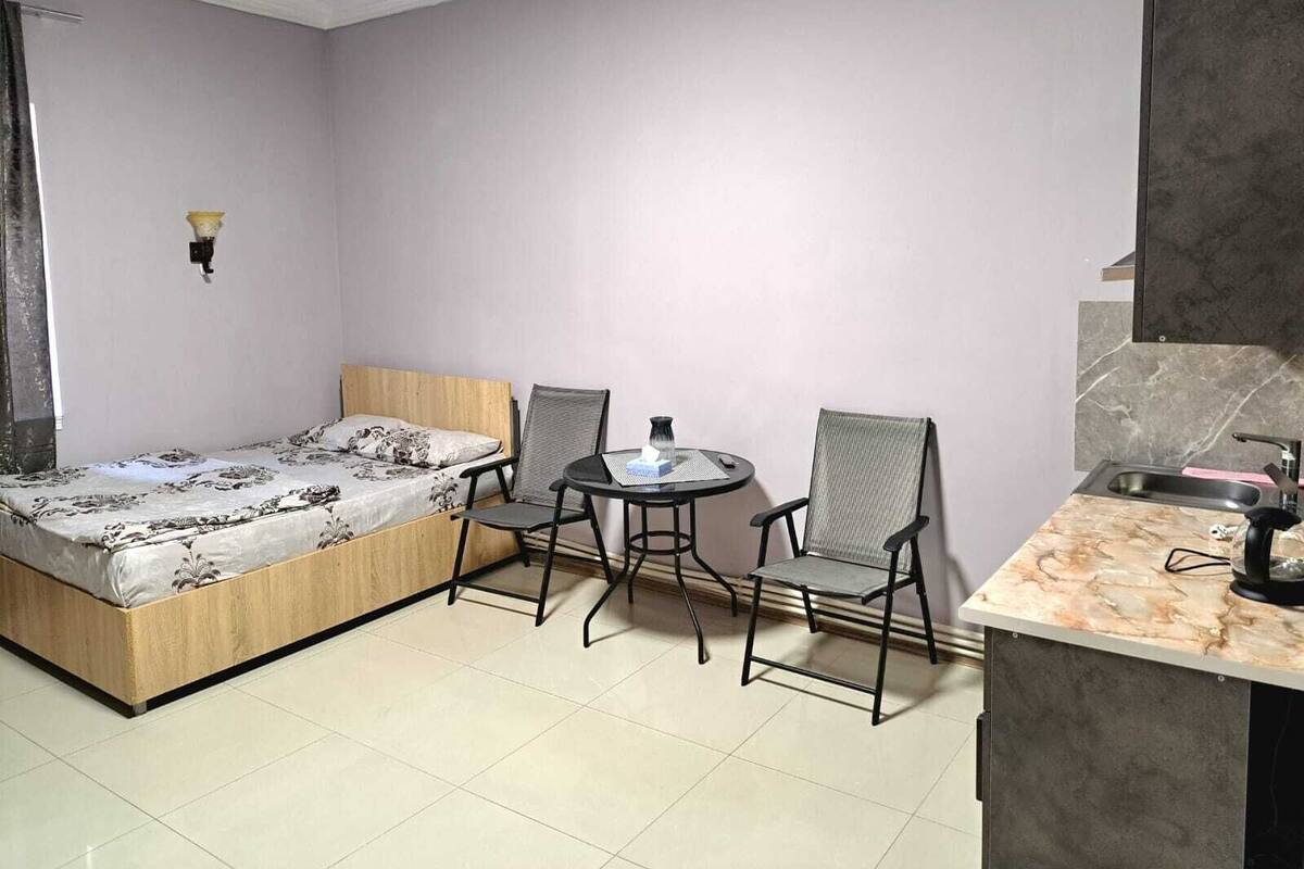 Ein kleines Zimmer mit einem Bett, zwei Stühlen, einem kleinen runden Tisch, einem Waschbecken und einem Spiegel.