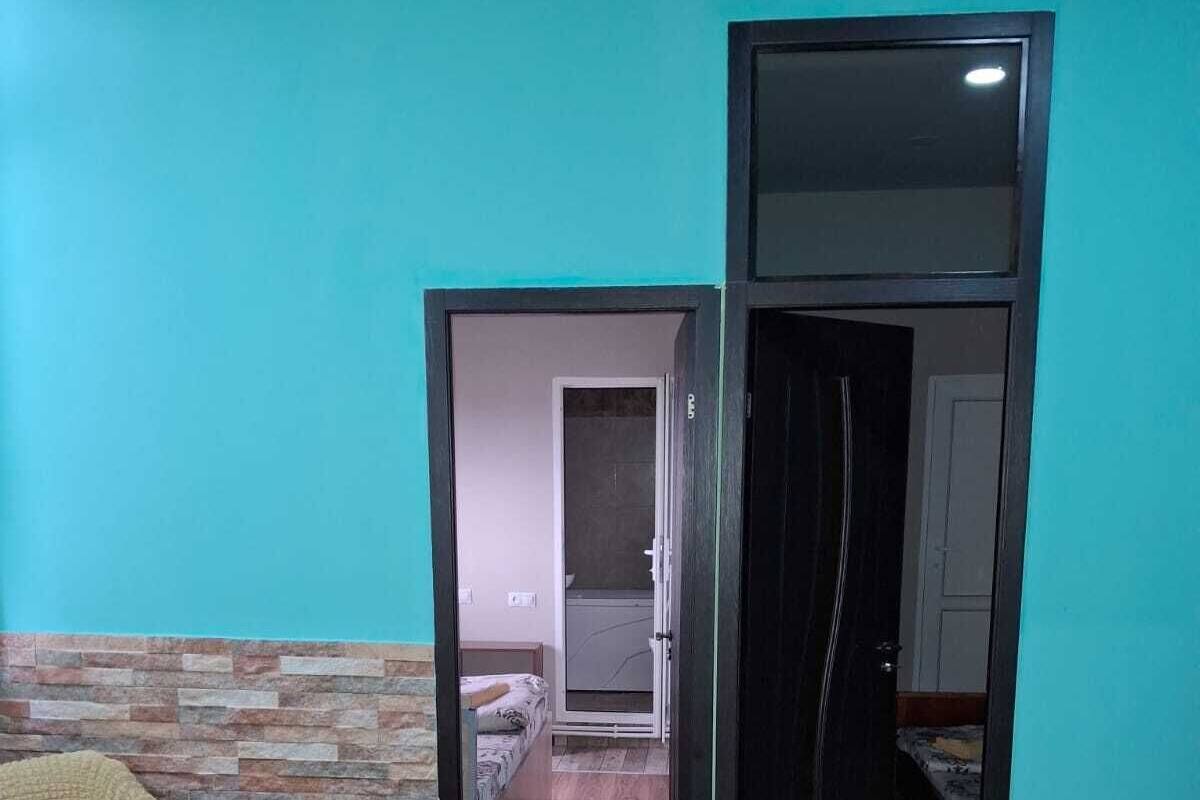 Ein Zimmer mit einem Bett, einem Sessel, einem kleinen Tisch und einem Durchgang zu einem anderen Raum.