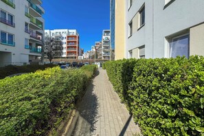 Ein Weg, gesäumt von ordentlich geschnittenen Hecken, der zu einer Reihe mehrstöckiger Wohnhäuser mit Balkonen führt.