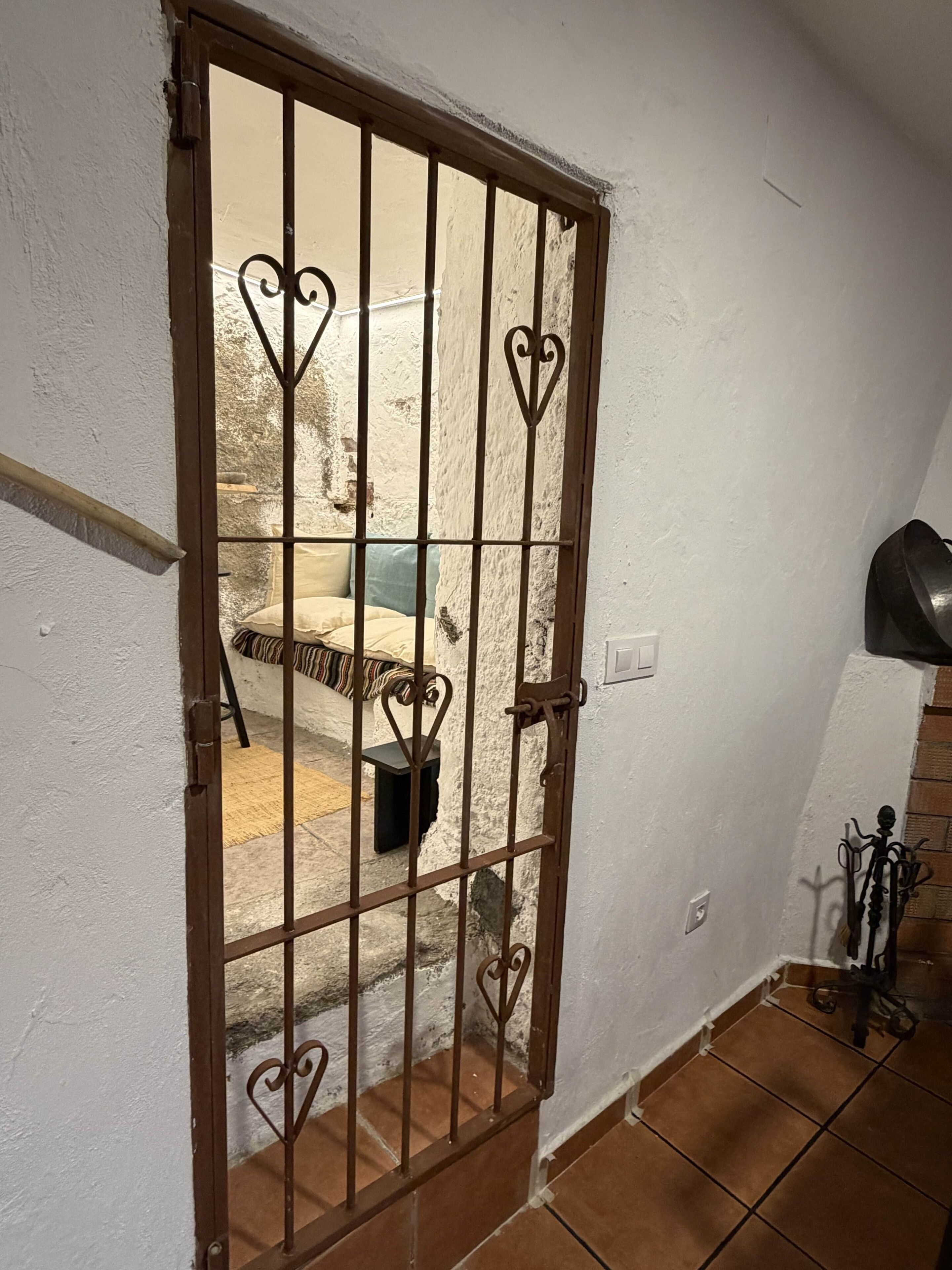 A room with a barred door, a small table, a chair, and a bed with a striped blanket.