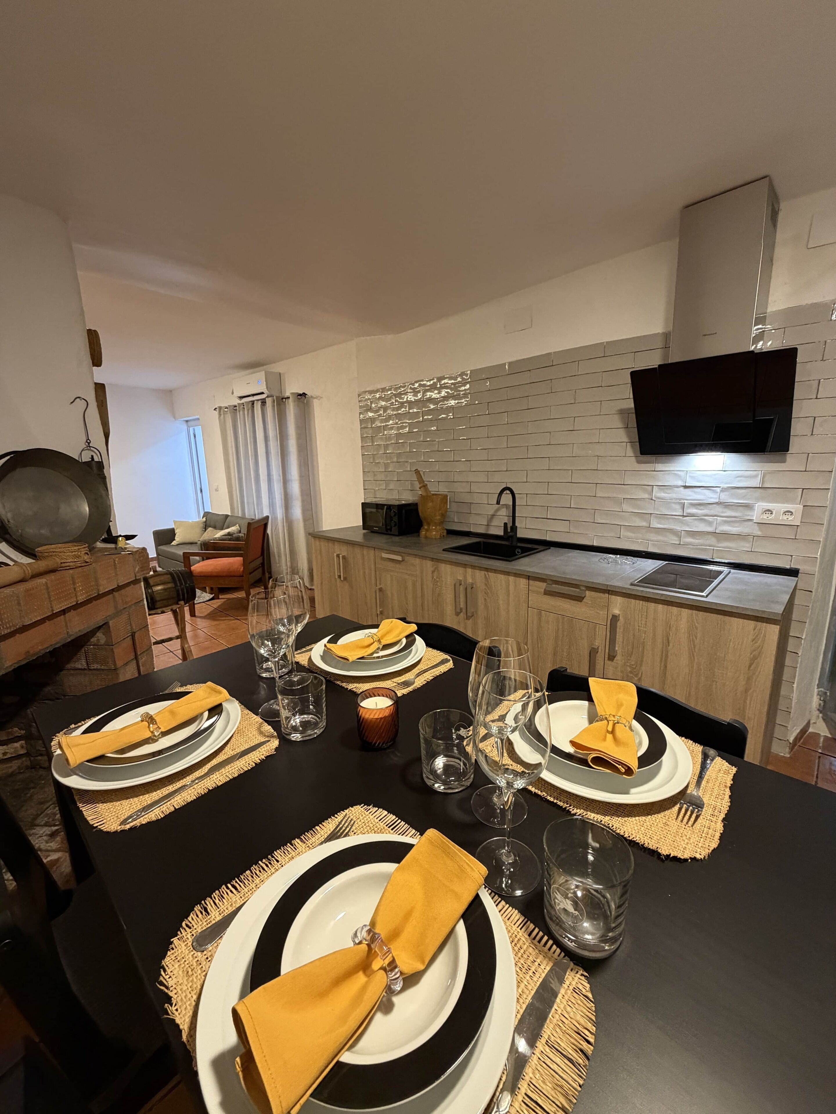 Comedor con una mesa negra dispuesta para cuatro personas, incluyendo platos, cubiertos y servilletas.