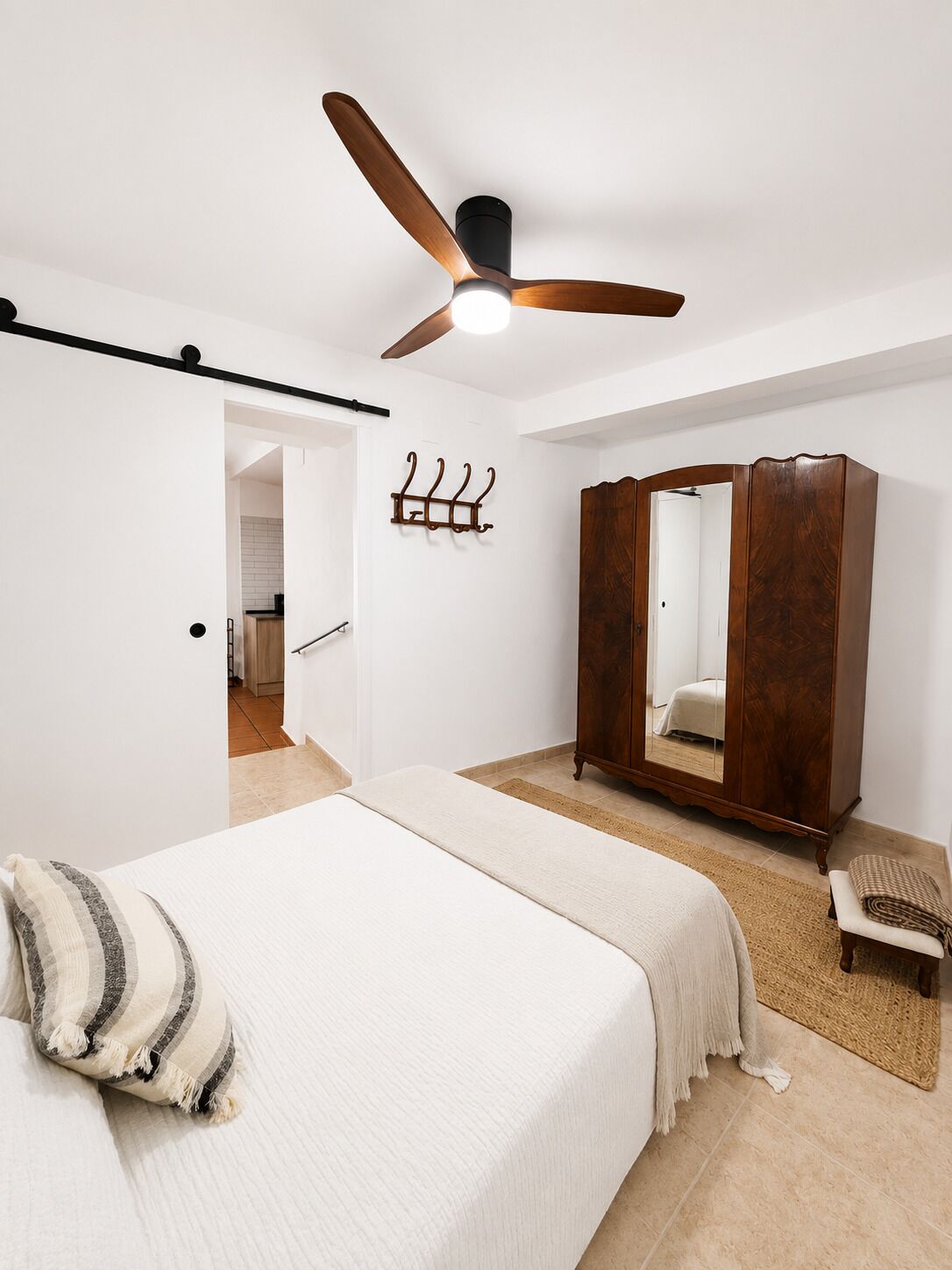 Un dormitorio con cama, armario de madera, ventilador de techo y perchero.