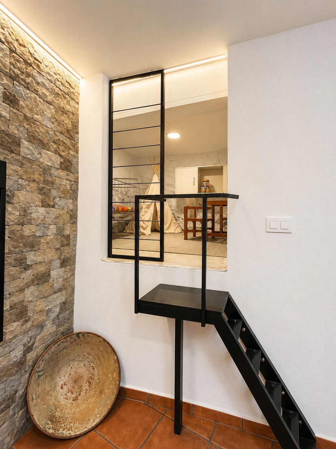 A modern staircase with a black metal railing, a stone wall, and a rustic woven basket on the floor.