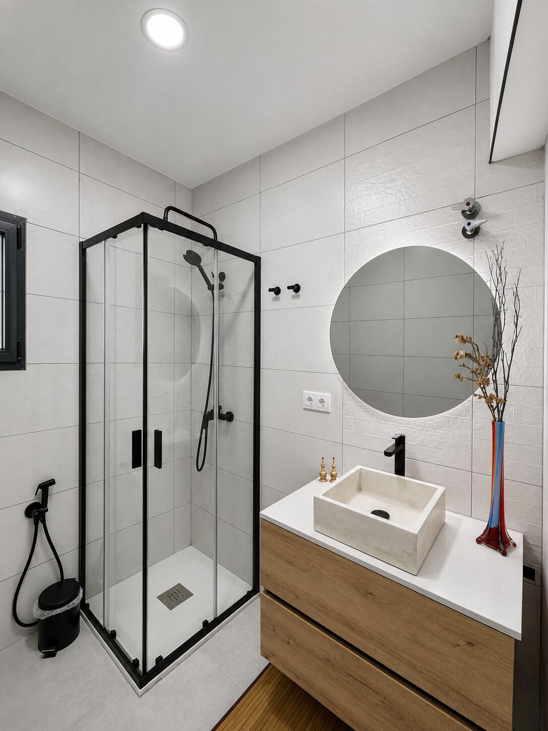 A modern bathroom with a glass-enclosed shower, a round mirror, and a wooden vanity with a sink.