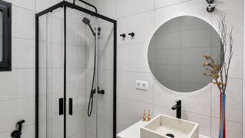 A modern bathroom with a glass-enclosed shower, a round mirror, and a wooden vanity with a sink.