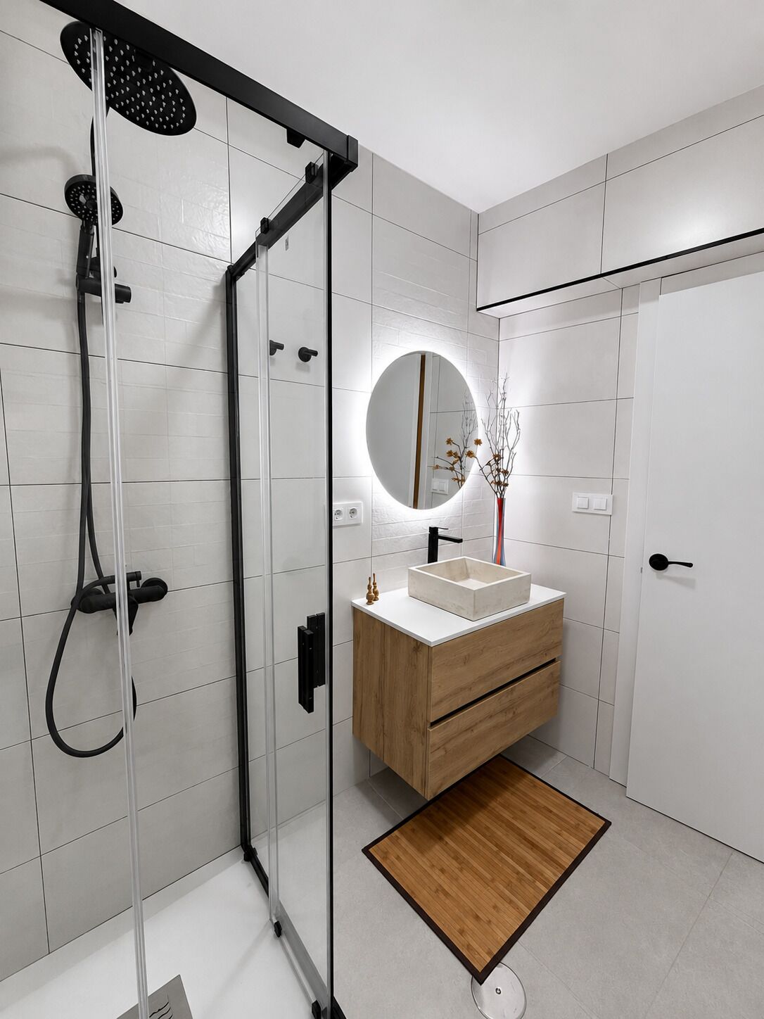 Un baño moderno con ducha de vidrio, espejo redondo y tocador de madera.