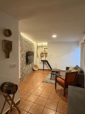 A living room with a stone wall, a TV, a wooden table, and a sofa. - La Casa de la Abuela - El Mirador de Gérgal (Almería)