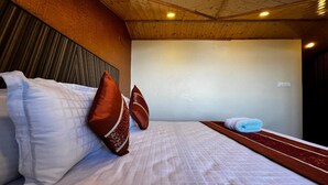 A hotel room with a bed, pillows, a wooden headboard, a white wall, and a ceiling with wooden beams.